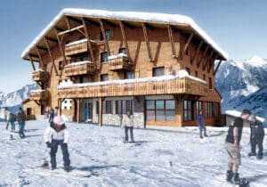 Grand chalet en bois avec neige sur le toit et balcons, au pied d'une montagne. Des snowboarders profitent de la neige au premier plan.